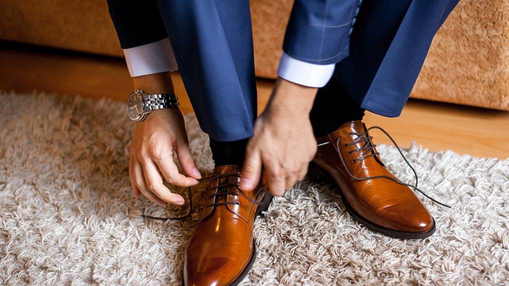 A man ties up his shoelaces on his brown shoes