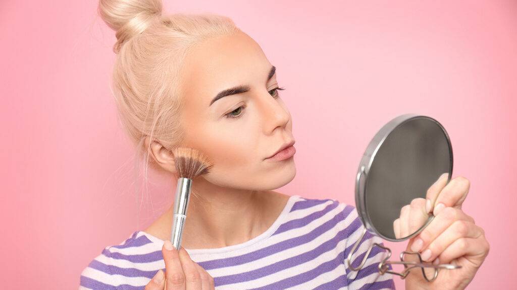 can-i-use-any-foundation-with-an-airbrush-machine-blonde-woman-applying-foundation-pink-backdrop